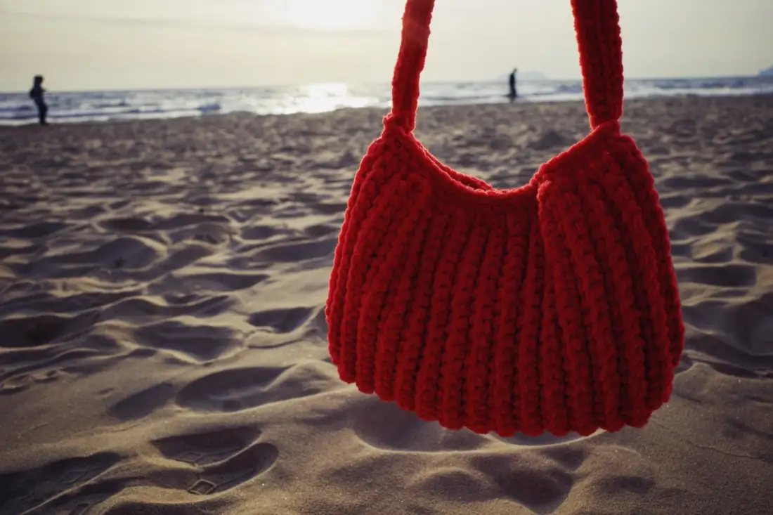 Borsa rossa all’uncinetto in controluce sulla spiaggia al tramonto